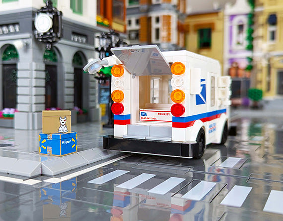 LEGO mail truck and delivery boxes being delivered in a brick built lego city, blurred lego buildings in the background.